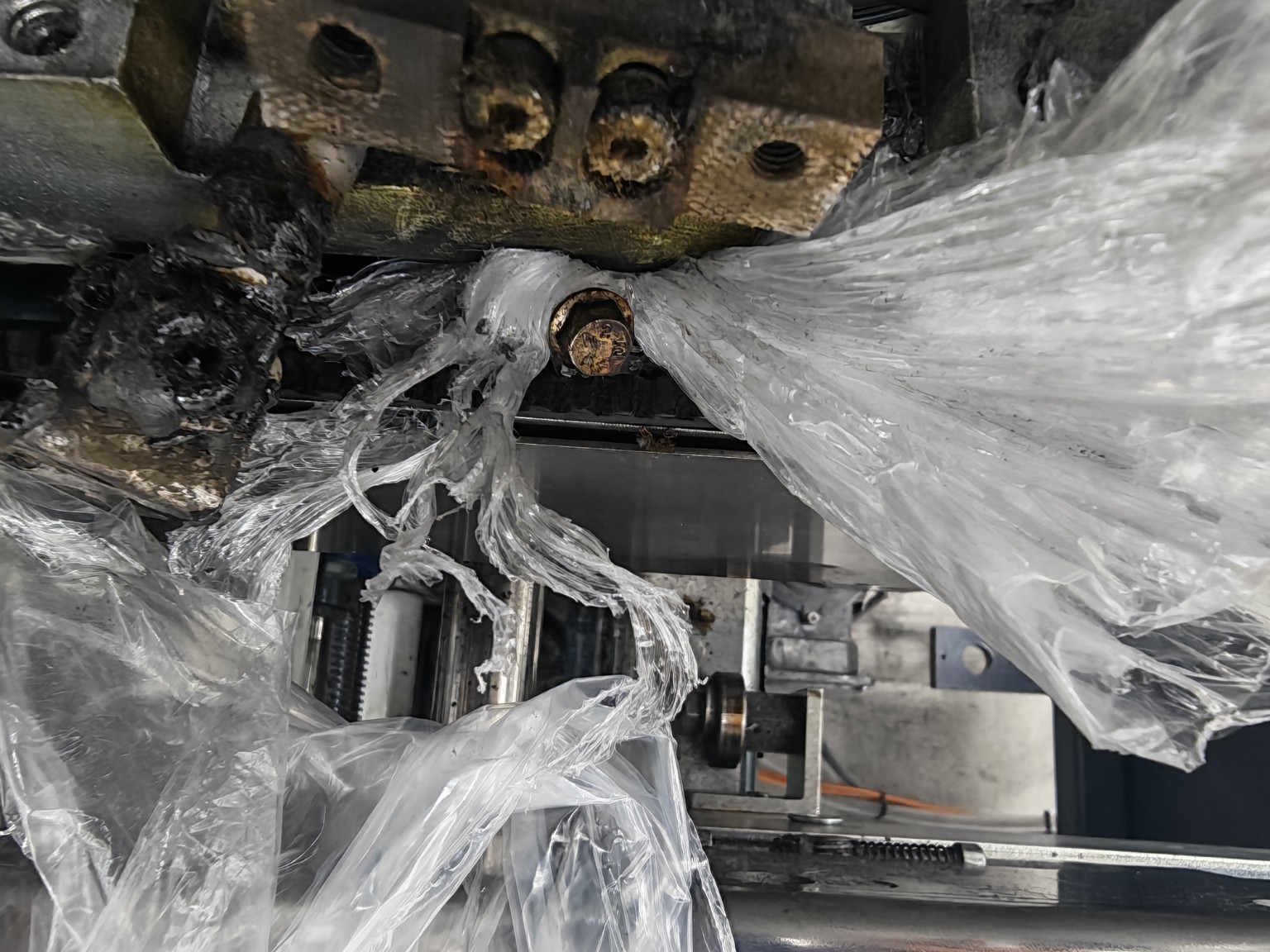 Production sealer film-feed area showing plastic jammed around the sealing assembly during an SLW Engineering breakdown investigation.
